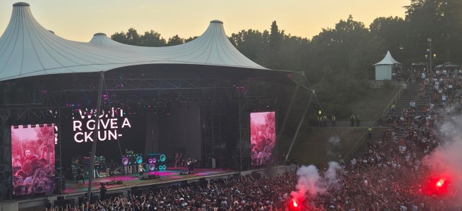 Die fünf Musiker der US-amerikanischen Rockband Limp Bizkit performen auf der Konzertbühne der Berliner Wuhlheide bei Abendlicht, der Innenraum vor der Bühne ist mit hunderten Menschen dicht befüllt, es sind zwei gezündete Bengalische Feuer in roter Farbe zu sehen.