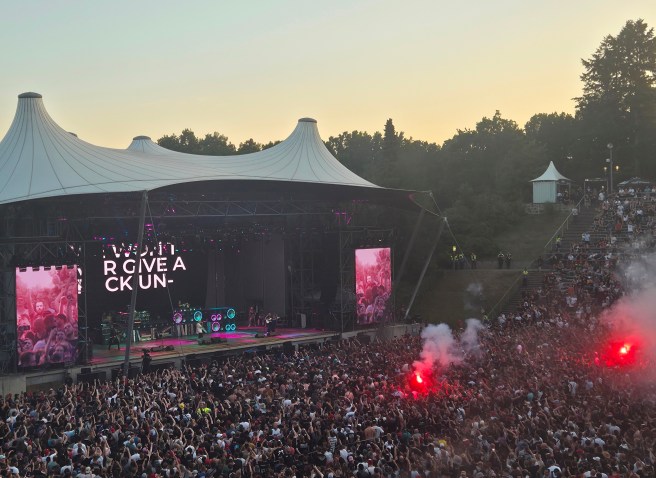 Die fünf Musiker der US-amerikanischen Rockband Limp Bizkit performen auf der Konzertbühne der Berliner Wuhlheide bei Abendlicht, der Innenraum vor der Bühne ist mit hunderten Menschen dicht befüllt, es sind zwei gezündete Bengalische Feuer in roter Farbe zu sehen.